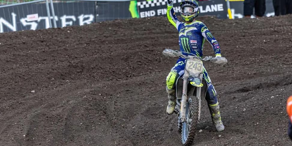 A Monster Energy-liveried factory Yamaha carrying number board 243 riding back up the track with one hand raised, an END FINISH LANE board on the fence behind